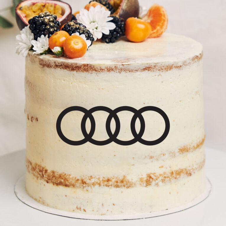 White cake with berries and passionfruits next to a plant behind a white background